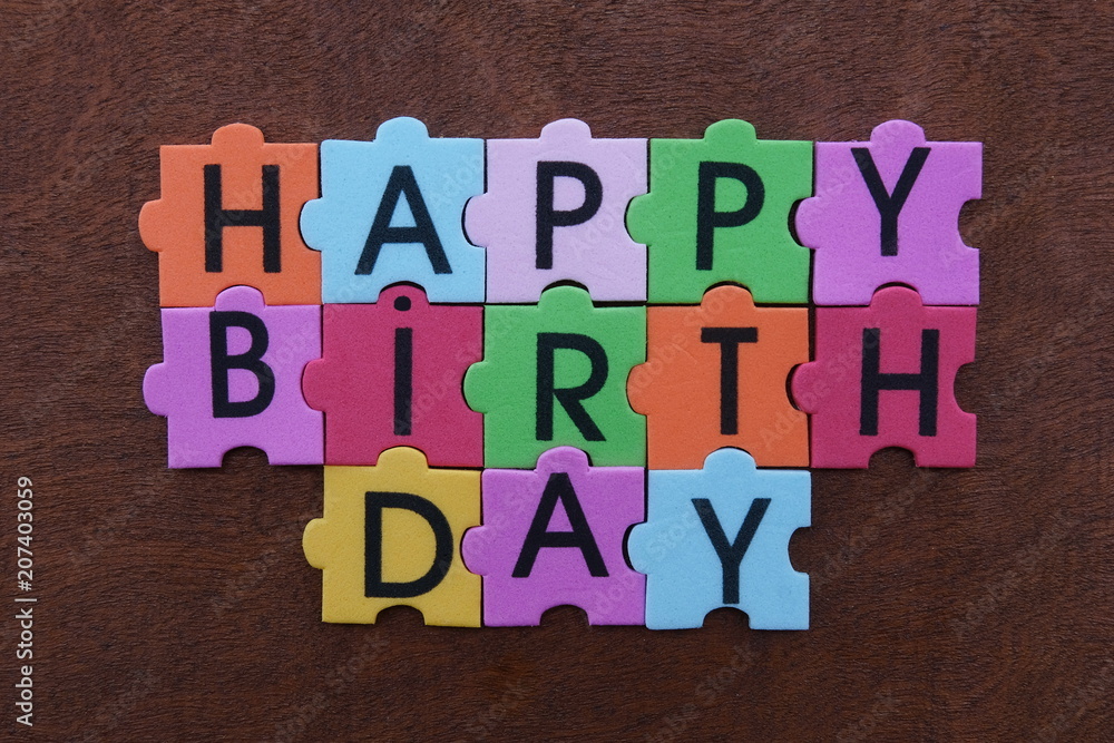 Happy Birthday text with multicolored puzzle letters over a wooden board Happy Birthday text with multicolored puzzle letters over a wooden board