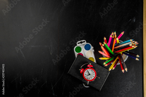 Back to school concept with books, alarm clock, color pencils, chalkboard background