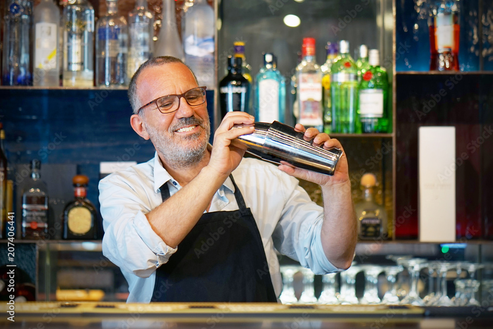 Professional elderly bartender man holding in hands a shaker with a fresh  delicious cocktail. Bartender shaking a cocktail shaker as she stands  behind the bar mixing a drink for a client. Photos