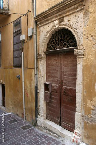 The old arch wooden door in the yellow stone house on the small pedestrianized paved street on the sunny day. © Anna Silanteva