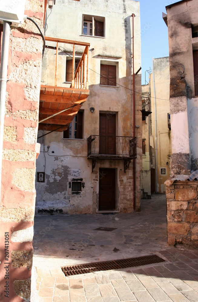 The small pedestrianized paved street among stone houses in the Mediterranean town on the sunny day. The small pedestrianized paved street among stone houses in the Mediterranean town on the sunny day.