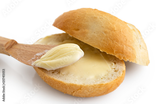 Fotografija Detail of butter spread on a cut crusty bread roll with a wooden knife isolated on white