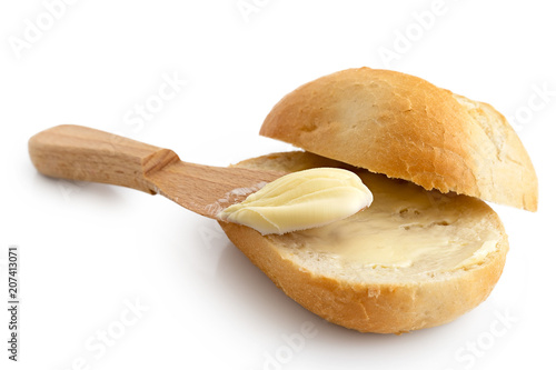 Butter spread on a cut crusty bread roll with a wooden knife isolated on white. photo