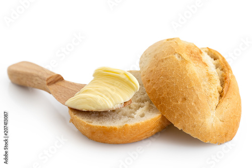 Butter on wooden knife resting on a cut crusty bread roll isolated on white.