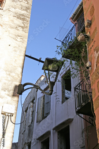 The old lamp, the plant and walls of abandoned houses with windows in the Mediterranean town on the sunny day. 