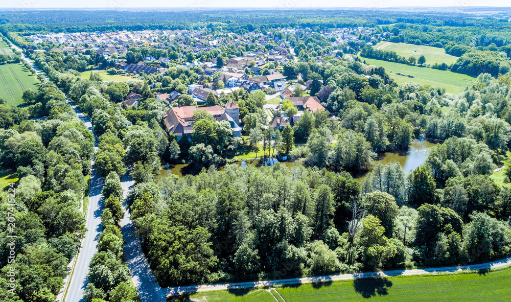 Aerial view of a German village with a small forest, a pond and a moated castle in the foreground