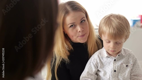 Close-up of a mother with a small son at a doctor's appointment, the doctor cute talking to the child. Little boy is afraid of the doctor. Portrait of a little boy patient with his mother at doctor. photo