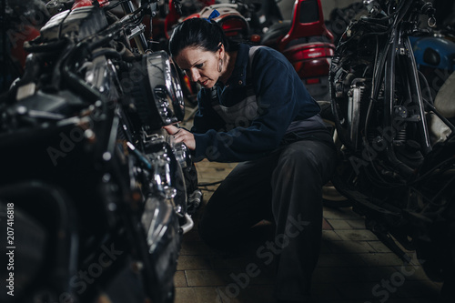 Strong and worthy woman doing hard job in car and motorcycle repair shop.