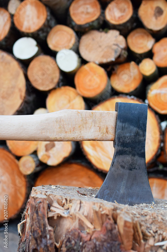 Steel axe and deck for cutting firewood on stack of tree logs background. Workplace for chopping firewood for winter.