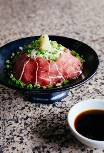 Japanese Tataki raw beef cuisine with ginger, onion, spring onion and soy sauce set on red wooden tray