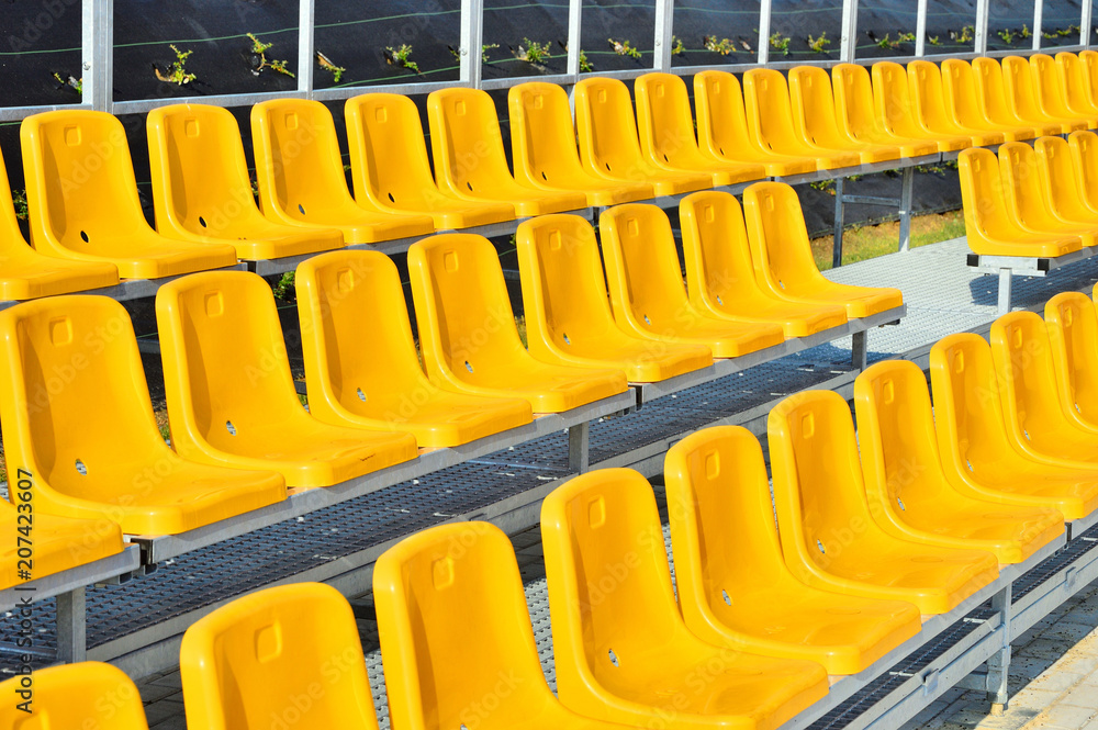 Żółte plastikowe krzesełka na trybunie stadionu sportowego. - obrazy, fototapety, plakaty 