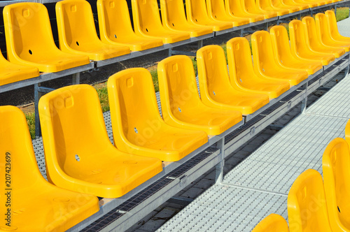 Żółte plastikowe krzesełka na trybunie stadionu sportowego.
