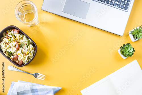 Vegetable salad with macaroni bowls with cheese in a container for lunch at the office workplace near the laptop. Top view, flat lay. Copyspace