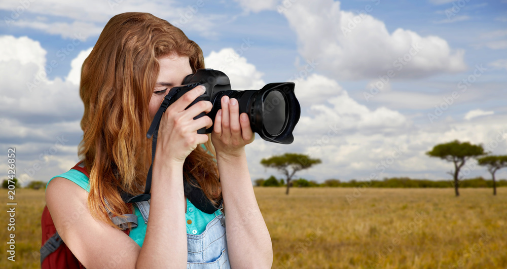 travel, tourism and photography concept - happy young woman with backpack and camera photographing over african savannah background