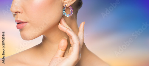 beauty, jewelry and luxury concept - close up of beautiful woman face with earring over pastel background