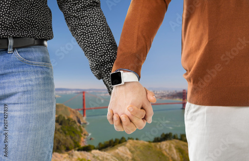 same-sex relationships, lgbt and technology concept - close up of male gay couple holding hands with smartwatch