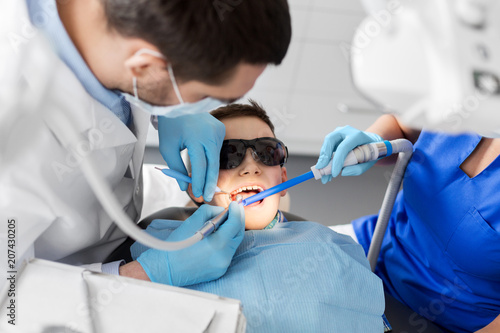 medicine  dentistry and healthcare concept - dentist and assistant with dental drill and saliva ejector treating kid patient teeth at dental clinic