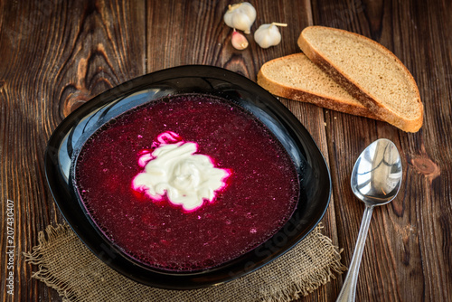 Traditional Belarusian, Russian or Ukrainian borscht with bread and sour cream on a wooden table.