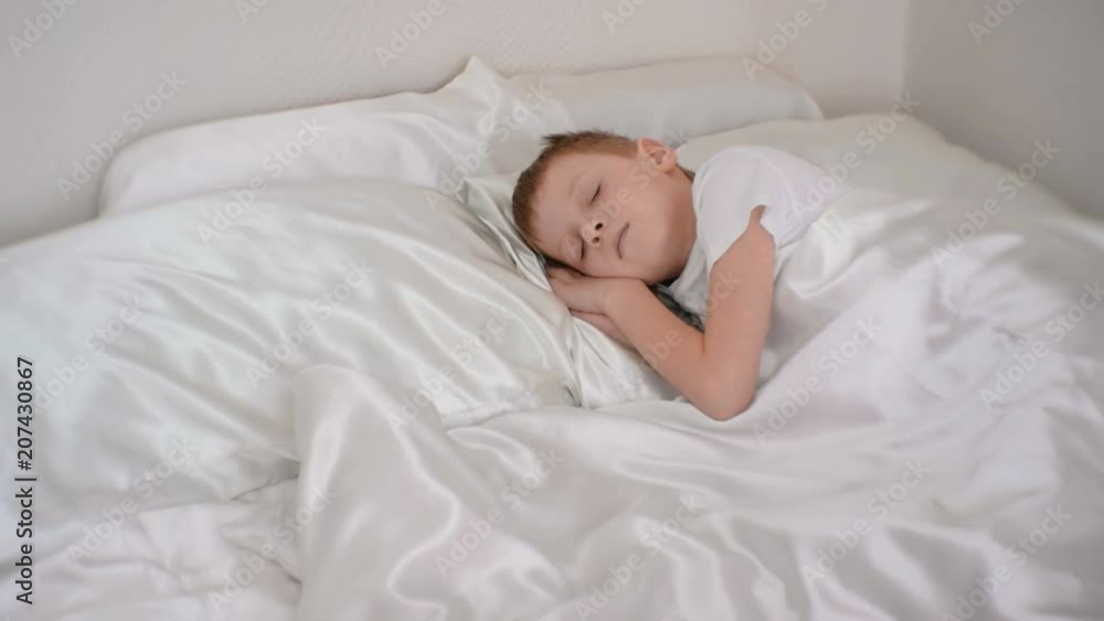 Seven-year-old a boy quietly sleeping in bed in his room, putting hands under his head. Seven-year-old a boy quietly sleeping in bed in his room, putting hands under his head.