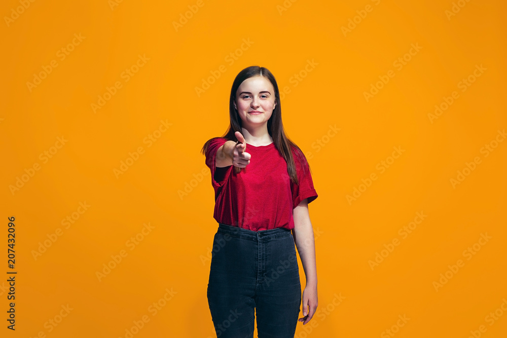 The happy teen girl pointing to you, half length closeup portrait on orange background. The happy teen girl pointing to you, half length closeup portrait on orange background.