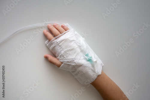 Kid hand with an elastic bandage with the tube of normal saline infusion.