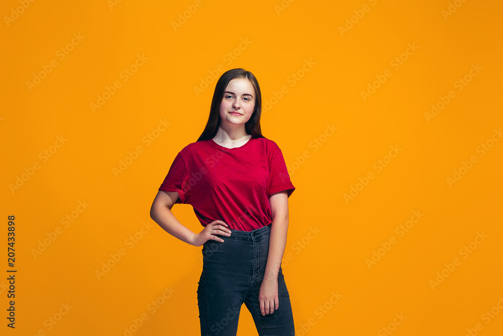 The happy teen girl standing and smiling against orange background. The happy teen girl standing and smiling against orange background.