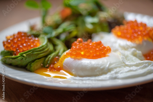Delicious breakfast with poached eggs, red caviar and sliced avocado