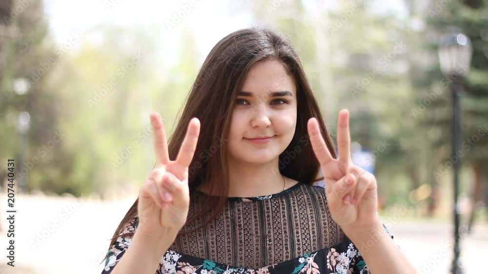 Young woman posing showing hand gesture victory on park background. Young woman posing showing hand gesture victory on park background.