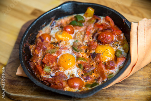 Shakshuka - eggs in tomato sauce in a skillet over wooden background.