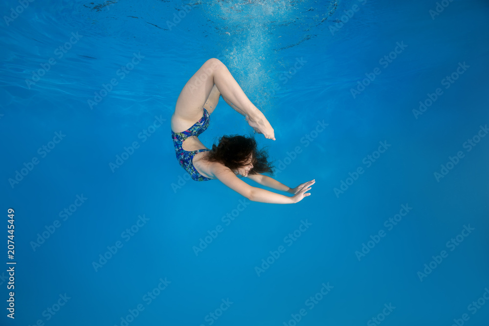 Girl curled into a wheel under water in the pool. Underwater acrobatics