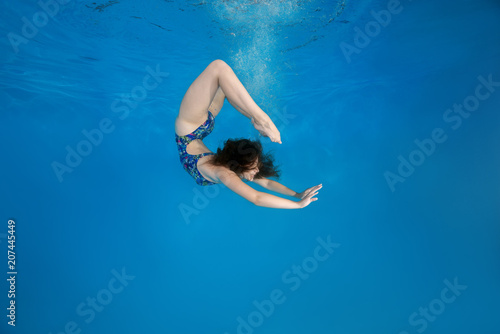 Girl curled into a wheel under water in the pool. Underwater acrobatics