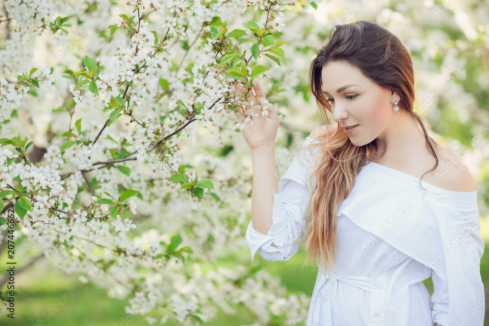 Young beautiful blonde woman in blooming almonds garden.