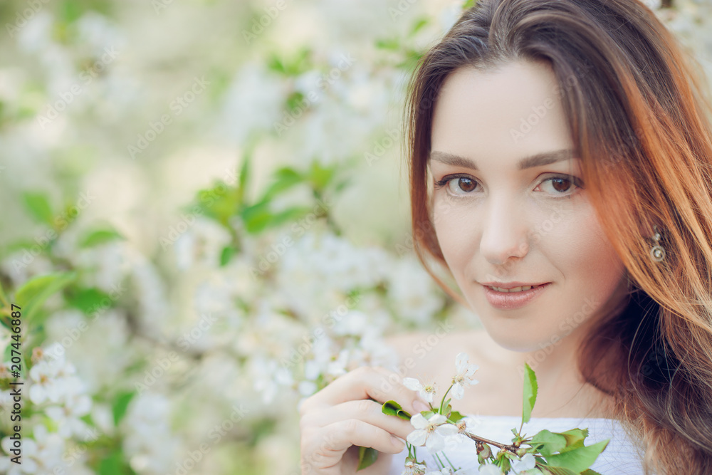 Fototapeta premium Young beautiful blonde woman in blooming almonds garden.