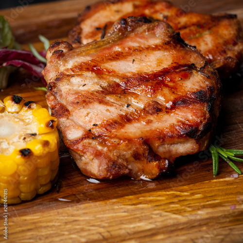 two grilled steaks with corn and salad on a wooden plank