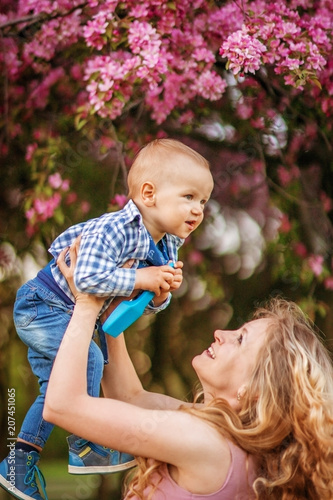 Mother, beautiful girl blonde woman, with a baby in her arms for a walk in a flower garden.
