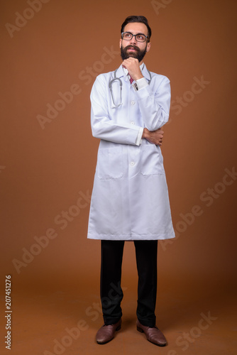 Young handsome bearded Persian man doctor against brown backgrou