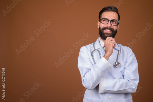 Young handsome bearded Persian man doctor against brown backgrou