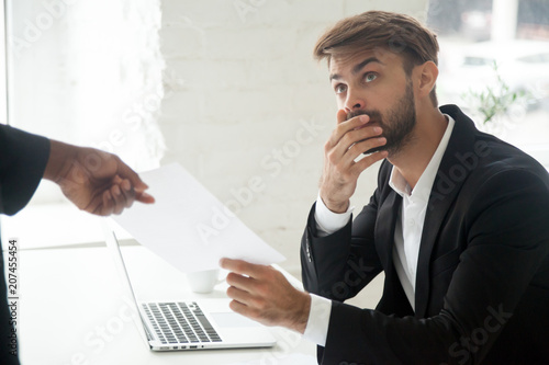 Frustrated shocked Caucasian male worker getting dismissal notice from African American boss asking to leave workplace. Employee receiving unexpected termination letter. Concept of firing, career end
