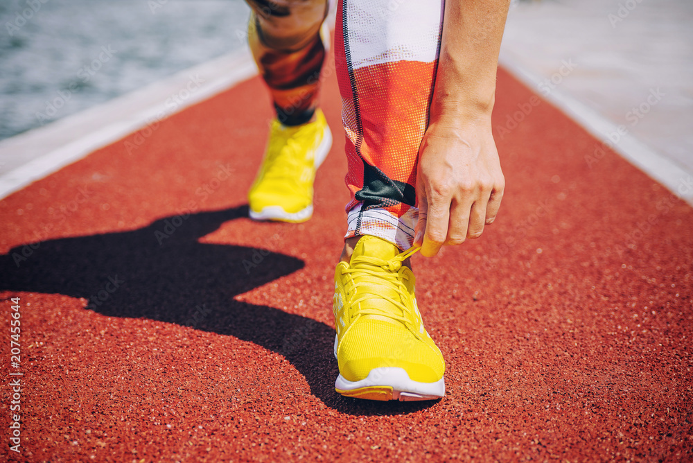 Fototapeta premium Woman tying jogging shoes. Great running outdoors on a sunny day.