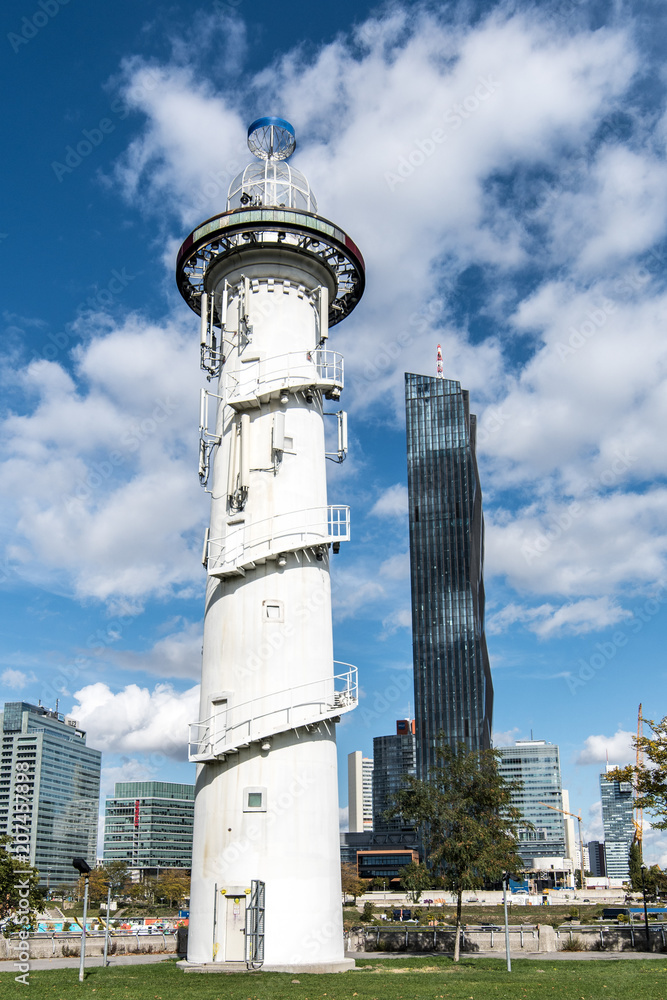 Donauinsel Lighthouse, Vienna, Austria on a sunny day with white clouds floating in the sky and a cityscape background. Donauinsel is a man made island as part of flood defences on the Danube River. Donauinsel Lighthouse, Vienna, Austria on a sunny day with white clouds floating in the sky and a cityscape background. Donauinsel is a man made island as part of flood defences on the Danube River.