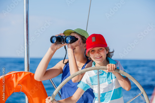 Boy captain with his sister on board of sailing yacht on summer cruise. Travel adventure, yachting with child on family vacation. © Max Topchii