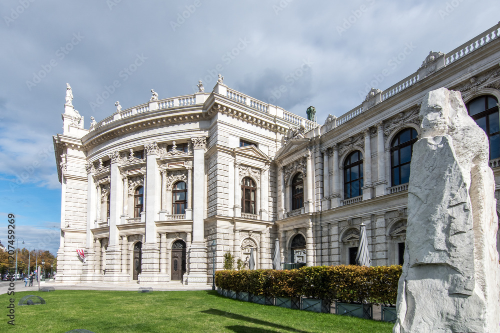 Classical, typical Viennese architecture in the middle of the old city centre, with white clouds and blue sky above. A large rock forms an additional focal point in the foreground of the frame