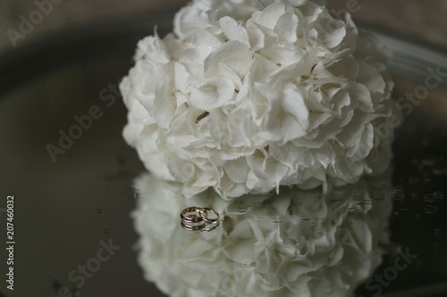 A bouquet of white hydrangeas and engagement rings lie on a glass table. Close-up horizontal photo