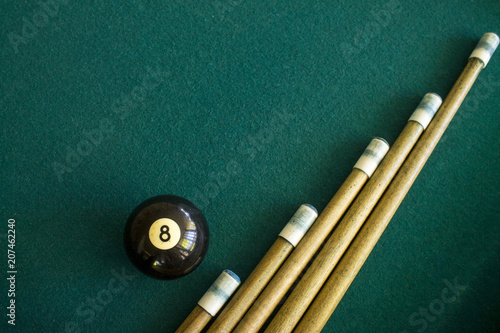 Eight black billiard ball on a green billiard table next to a group of a cue sticks photo