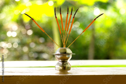 Burning orange incense joss stick on a holder with green background
