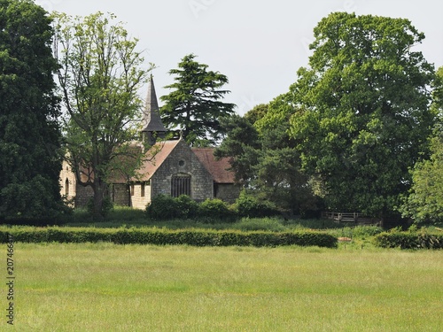 Acaster Malbis village church near York nestled amongst trees viewed across a green field in spring