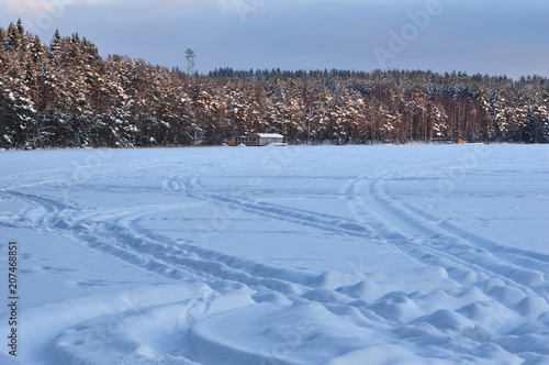 Snowmobile trail on a snowy frozen lake against the forest.