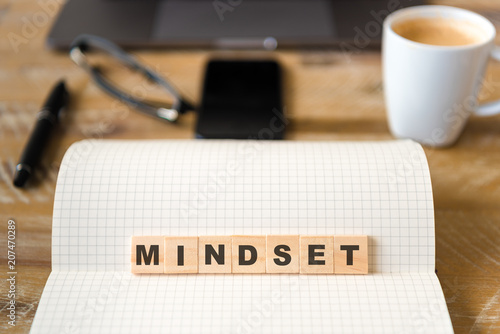 Closeup on notebook over wood table background, focus on wooden blocks with letters making Mindset text
