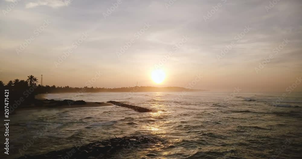 Drone flying right over incredible sunset ocean coast. Amazing aerial panorama of sun setting above waves reaching shore Drone flying right over incredible sunset ocean coast. Amazing aerial panorama of sun setting above waves reaching shore