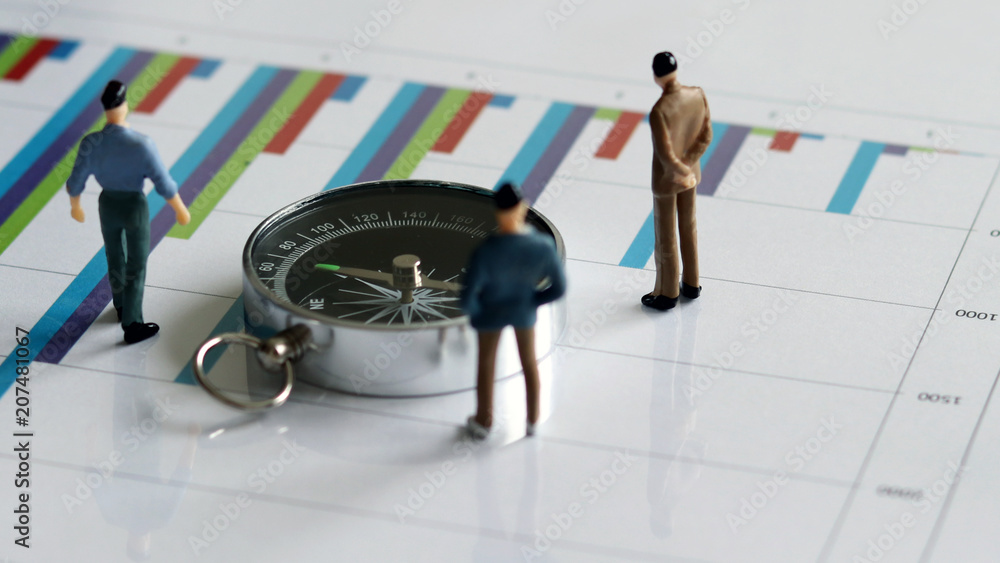 Fototapeta premium appearance from behind of compass and three miniature men on the chart